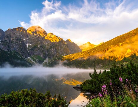 Mountain scene reflects in lake under a cloudy blue sky during golden hour