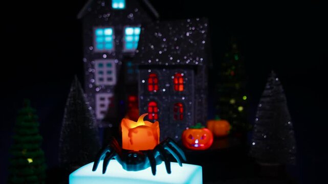 A candle in a spider candlestick on a stand moves against the backdrop of a Halloween village with black houses and bright pumpkins 