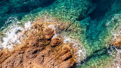 Panoramic aerial view of a cove between Esterel Mountains red cliffs with a board on the water, Mediterranean Sea, French Riviera, Southern France, scenic coastline, turquoise water
