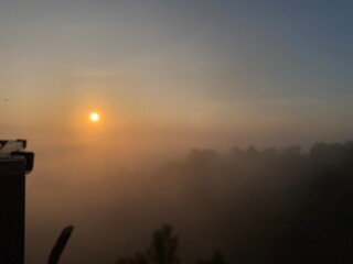 grassy mountain slope with a wooden fence, lit by morning sun. Tall evergreen overlooks hazy valleys. moody winter sunset over the Cotswold countryside. Sunlight on the morning with sea of fog.