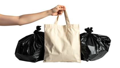 Hand holding a tote bag centered between two black trash bags, isolated on black