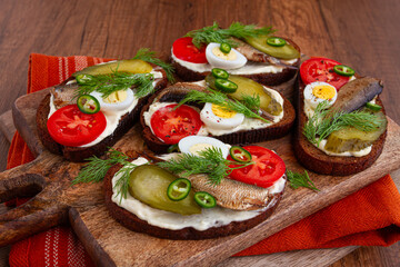 open sandwiches with sprats, vegetables and herbs, on a wooden board, breakfast, snack,
