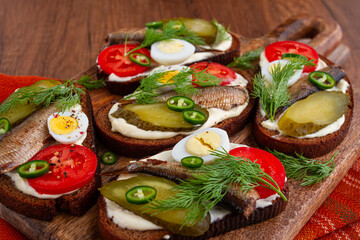 open sandwiches with sprats, vegetables and herbs, on a wooden board, breakfast, snack,
