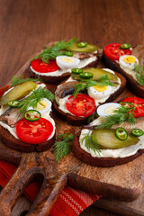 open sandwiches with sprats, vegetables and herbs, on a wooden board, breakfast, snack,