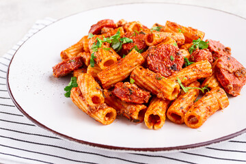 rigatoni pasta with spicy sausage, and rich tomato sauce served, on a white plate, homemade,