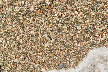 Natural beach texture with tiny stones and gentle surf, ideal for seasonal designs. Small stones and pebbles shaped by water action over time. smooth textures and patterns-Natural shaping of shore.