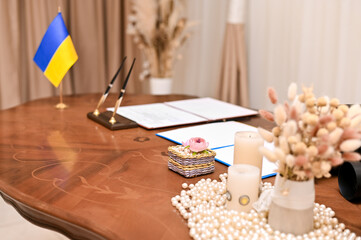 Wooden desk in Ukrainian registry office small national flag, stacks of official papers, pen. solemnity of administrative space. Close-up symbolic arrangement on registry office desk, Ukrainian flag