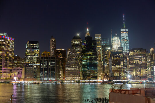 Nighttime view of Manhattan's skyline from the Brooklyn Promenade, showcasing illuminated skyscrapers along the East River of the NYC Skyline in the Financial District