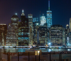 Nighttime view of Manhattan's skyline from the Brooklyn Promenade, showcasing illuminated skyscrapers along the East River of the NYC Skyline in the Financial District