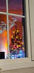 A lit Christmas tree with Christmas decorations through a window inside a house immersed in the Christmas holidays