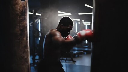 Muscular african american boxer training in a dark gym. A strong fighter punching with red gloves during an intense workout. Strength and motivation concept - Powered by Adobe