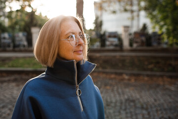 Smiling senior woman 55-60 year old wearing glasses outdoors. Stylish middle age female.
