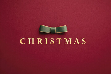 Burgundy Christmas background textured paper with gold typography, green bow. Clean, luxurious flat lay with generous copy space. Banners, ads, website headers, posters, greeting cards, branding.
