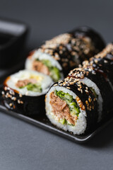 Sushi roll with salmon,  avocado and tuna wrapped in nori seaweed. Sushi set served on the black plate next to red ginger with black sticks on the black background.