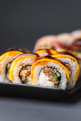Sushi roll with salmon,  avocado and tuna. Sushi set served on the black plate next to red ginger with black sticks on the black background