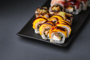 Sushi roll with salmon,  avocado and tuna. Sushi set served on the black plate next to red ginger with black sticks on the black background