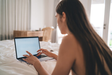 Freelance woman working on laptop while lying on bed, immersed in remote digital tasks,...