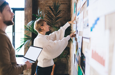 Female freelancer collaborates on wall strategy with male coworker, planning digital concept...