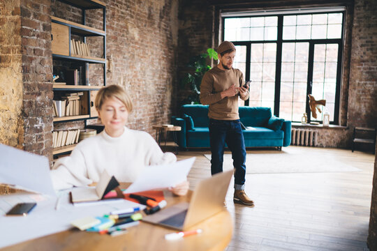 Freelancer woman sorts UX sketches while male coworker checks mobile app, showing balance of analog and digital tools in collaborative design studio. - Powered by Adobe