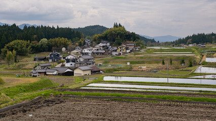 Scenic view of rural Japan with traditional houses and terraced rice fields under a cloudy sky