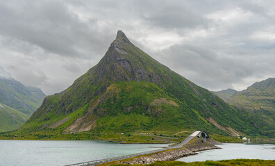 Scenic view of steep mountain peak and bridge in a coastal landscape during overcast conditions.