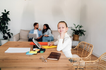 Girl smirks while watching parents talk on sofa, blending childhood confidence and emotional awareness in modern home environment with visible tech use.
