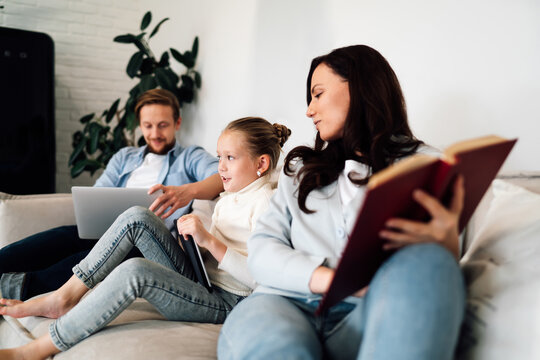 Girl animatedly responds to something on tablet while mother holds book and father works, reflecting real-time interaction across mixed media formats.
