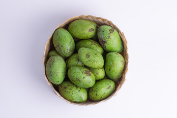 Flat lay of raw green mangoes in a traditional round bamboo basket on white background. Perfect for tropical cuisine, healthy eating, traditional market, and sour fruit recipes.
