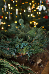 Making Christmas wreath. Christmas wreath with fir, pine and cedar branches, scissors on wooden table on background of stylish xmas tree. Winter holidays preparation and decor