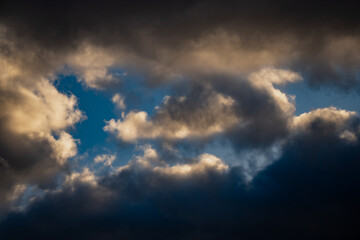 Obraz premium Moody sky with layers of bright and shadowed clouds showing deep blue gaps and soft evening light creating powerful natural contrast and atmospheric beauty