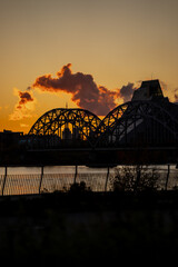 Sunset view of Riga with arched bridge and Daugava River creating warm reflections, city skyline...