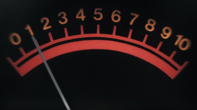 Macro view of a thin needle fluctuating across a vintage analog meter's red arched scale with orange numbers from 0 to 10, indicating signal level against a black background.