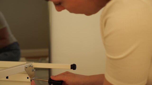 Close-up of woman&rsquo;s hands assembling flat pack furniture with screwdriver, tightening screw into wooden panel. DIY home improvement, self-assembly and modern lifestyle concept.