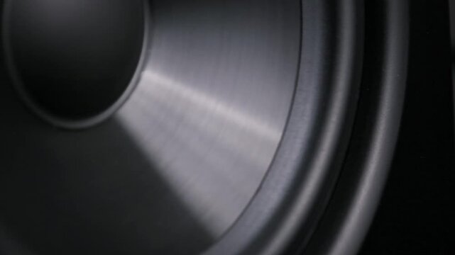 Extreme close-up pulsating black woofer cone membrane moving from powerful bass sound waves. Showing dynamic rubber surround details of hi-fi audio system component in motion.