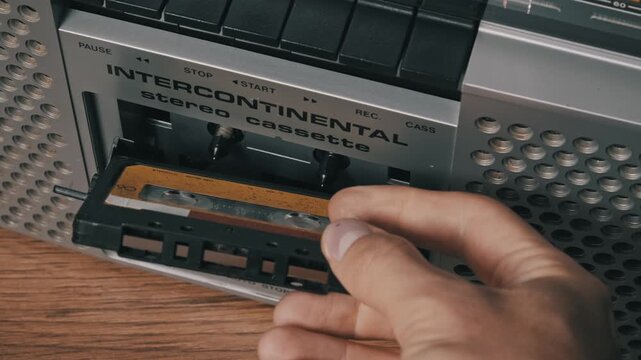 Close-up view hand ejecting and removing vintage audio cassette from silver boombox. Tape door opens, old tape is taken out, and door is closed manually.