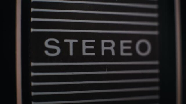Extreme close-up on retro stereo system red indicator light blinking on and off. Sign has textured, reflective background with white lettering for word STEREO in dark setting.