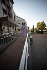 Obraz premium Stylish woman in a purple dress poses confidently on a railing outside a modern building, showcasing urban fashion and contemporary architecture in a vibrant city setting