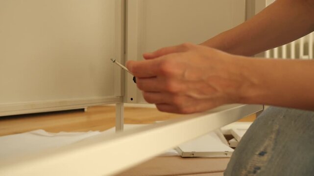 Close-up of woman&rsquo;s hands assembling flat pack furniture with screwdriver, tightening screw into wooden panel. DIY home improvement, self-assembly and modern lifestyle concept.