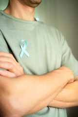 Close up of man with blue satin ribbon on shirt and crossed arms. Symbol of prostate cancer...