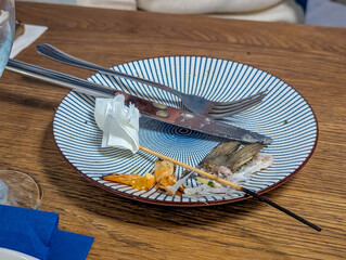 Clean striped blue and white plate with minimal food remains and napkin on wooden restaurant table surface. High quality photograph