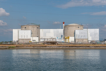 Industrial nuclear facility by waterfront under clear sky with distant clouds and power lines