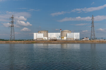 Industrial nuclear facility by waterfront under clear sky with distant clouds and power lines