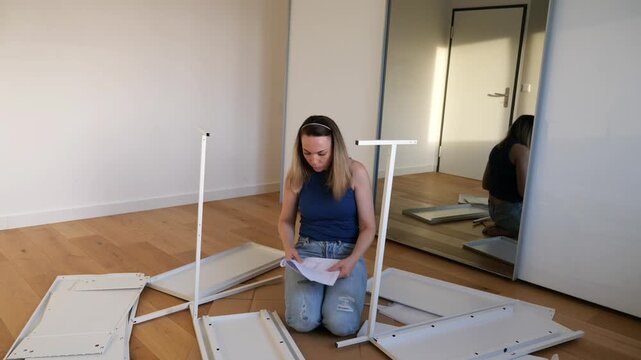 Young woman assembling flat pack furniture at home, sitting on floor with instruction manual, tools and parts around. DIY interior setup, modern lifestyle and home improvement concept