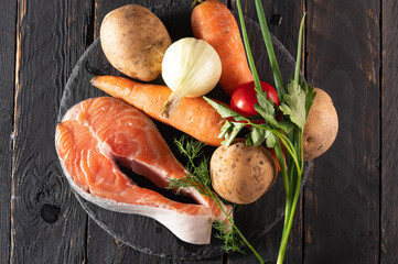 Modern culinary still life. Raw fish and veggies on stone and dark timber.
