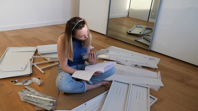 Young woman assembling flat pack furniture at home, sitting on floor with instruction manual, tools and parts around. DIY interior setup, modern lifestyle and home improvement concept
