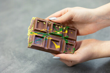 Female hands breaking off piece of Dubai chocolate on gray background. Green kadayif and pistachio spread with pistachio in trend dessert. Close-up, selective focus. High quality photo