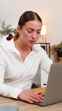 Young businesswoman at home office stares at frozen laptop presses keys and waits tense with sigh. Freelancer girl at table tries restart holds power key tests touchpad and looks for quick fix again.