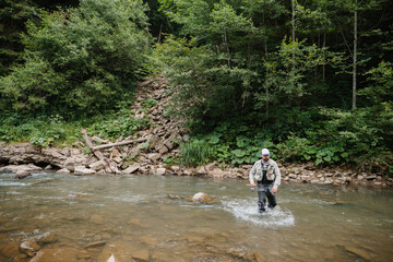 Fototapeta premium Fisherman wading in river, enjoying trout fishing in nature