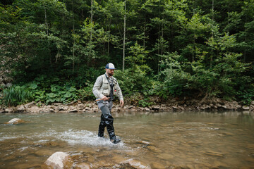 Fisherman wading in river, enjoying trout fishing in nature