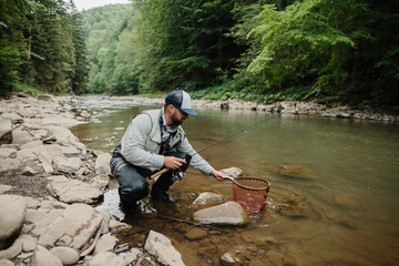 Fisherman catching trout in river with fishing net